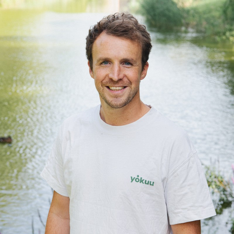 Man wearing a white t-shirt with 'yokuu' logo in a natural setting